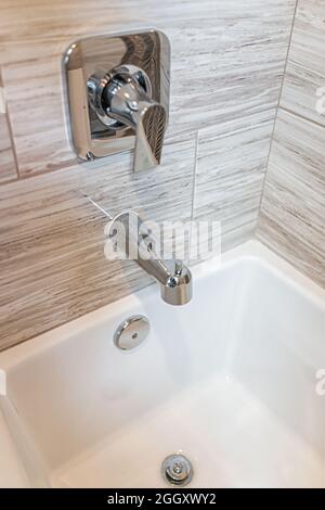 Nahaufnahme der neuen weißen modernen gekachelten Dusche mit Badewanne Badewanne Badewanne mit Edelstahl Wasserhahn Griffe und Abflussloch im Haus Modell Inszenierung zeigen Stockfoto