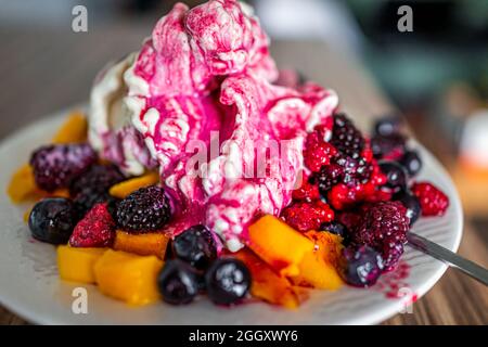 Makro-Nahaufnahme von bunten Schüssel weißen Teller Vanillebanane veganes Eis mit gefrorenen Heidelbeeren, roten Himbeeren und Mango mit sp gekrönt Stockfoto
