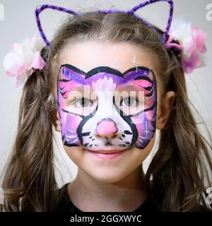 Kind mit Gesichtsbemalung von Kitty, nettes kleines Mädchen mit gemalter Maske auf ihrem Gesicht der Regenbogenkatze. Portrait von hübschen Kind mit schönen Make-up, einzigartig Stockfoto