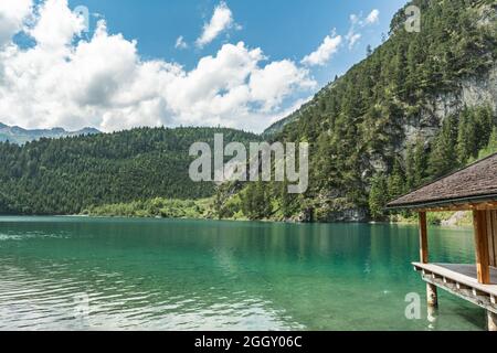 Ein Bootsschuppen und Blick auf einen smaragdgrünen Blindsee, umgeben von Wald und Bergen Stockfoto