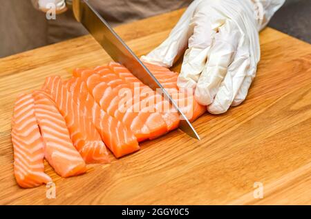 Die Hände des Küchenchefs aus nächster Nähe. Auf einem hölzernen Schneidebrett schneidet der Koch mit einem Messer einen roten Fisch. Stockfoto