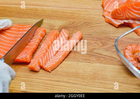 Die Hände des Küchenchefs aus nächster Nähe. Auf einem hölzernen Schneidebrett schneidet der Koch mit einem Messer einen roten Fisch. Stockfoto