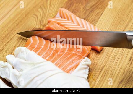 Die Hände des Küchenchefs aus nächster Nähe. Auf einem hölzernen Schneidebrett schneidet der Koch mit einem Messer einen roten Fisch. Stockfoto