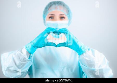 Eine Krankenschwester in einem medizinischen Gewand und einer Maske macht mit ihren Fingern eine innige Geste Stockfoto