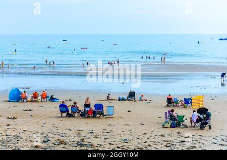 Gruppen sitzen am Saundersfoot Strand in Pembrokeshire, wales, während Familien im Meer hinter sich paddeln. Stockfoto