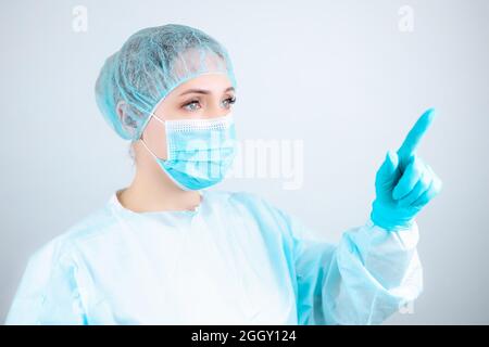 Eine Krankenschwester in einem medizinischen Gewand, einer Maske und Schutzhandschuhen steht seitlich und zeigt ihren Finger nach vorne Stockfoto