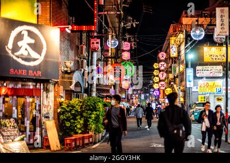 Osaka, Japan - 13. April 2019: Minami Namba Street mit Menschen, die in dunkler Nacht spazieren gehen und beleuchteten Neongebäuden mit roter Papierlaternen Sake Bar Stockfoto