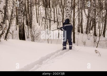 Der Mensch steht auf Skiern im Wald und zielt mit seiner Waffe die Schlucht hinunter. Ein Jäger oder Wilderer verfolgte Beute und zielte auf einen Schuss Stockfoto