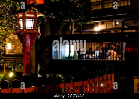 Kyoto, Japan - 16. April 2019: Gion-Viertel mit Kirschbäumen im Gartenpark und roter Laterne in der Nacht am Fluss und Hintergrund eines gehobenen Restaurants Stockfoto