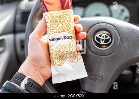 Greenville, USA - 7. Januar 2021: Eine Frau hält eine im Laden gekaufte Vanilleschokolade-Eisdiele von Haagen-Dazs und ein Schild mit dem Hintergrund der Autos Stockfoto