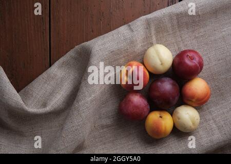 Saftige Früchte in einer Leinentischdecke auf einem alten Holztisch. Pflaumen, Aprikosen auf dunkelrotem Hintergrund. Draufsicht. Stockfoto