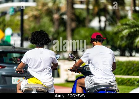 Miami Beach, USA - 19. Januar 2021: Zwei junge Männer fahren im Sommer auf der Stadtstraße in South Beach, Florida, auf italienischen Oldtimern Stockfoto