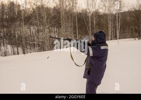 Ein Jäger oder Wilderer schießt im Winter eine Waffe, die Pulvergase werfen die Hülse aus und laden das Gewehr für den nächsten Schuss wieder auf Stockfoto