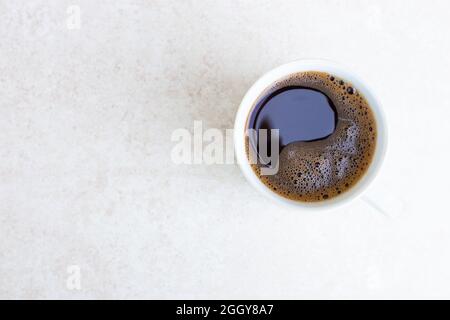 Weißer Becher mit frisch gebrühtem Kaffee auf einer hellen Tischfläche mit Kopierfläche, Draufsicht. Morgenerwachen, der Beginn eines neuen Tages. Starke invigor Stockfoto