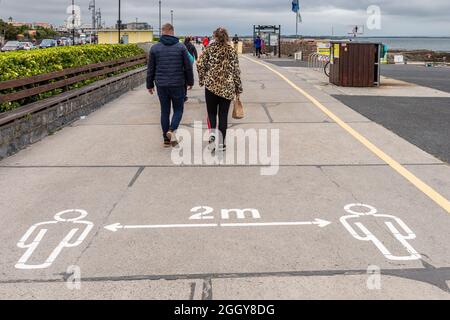 Die Menschen gehen an einem COVID-19 2m Schild an der Promenade in Salthill, County Galway, Irland, vorbei. Stockfoto