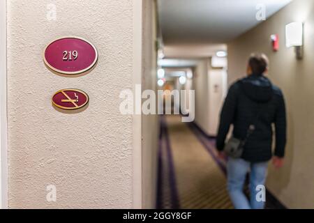 Nahaufnahme des Schildes im Inn Hotel Motel mit der Nummer für das Nichtraucherzimmer und ein Mann, der nachts auf dem Flur herumläuft Stockfoto