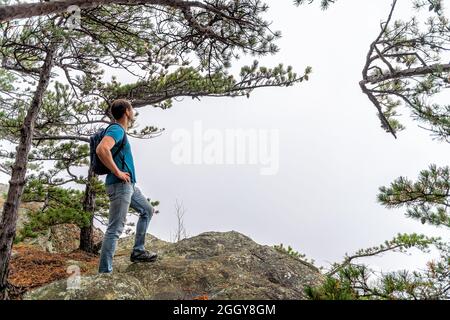 Blue Ridge Mountains im Herbst mit grünen Bäumen auf dem Berggipfel und einem jungen Mann, der auf einer Klippe am Cedar Cliffs in Virginia unterwegs ist, blicken auf die Berge Stockfoto