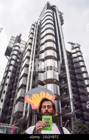 London, Großbritannien. September 2021. Ein Protestler mit einem Öl-befleckten Shell-Logo-Plakat hält während der Demonstration vor Lloyd's of London ein „Stop the Harm“-Flugblatt. Extinction Rebellion Demonstranten marschierten in der City of London im Rahmen ihrer zweiwöchigen Kampagne „Impossible Rebellion“ ein und forderten die britische Regierung auf, in der Klima- und Umweltkrise sinnvoll zu handeln. Kredit: SOPA Images Limited/Alamy Live Nachrichten Stockfoto