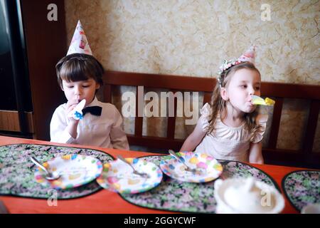 Kinderparty in Mützen feiert Geburtstag mit Kuchen und Ballons zu Hause. Stockfoto