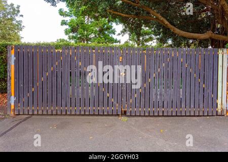 Verschlossenes Tor, das Mülltonnen vor einer Gartenhecke in botanischen Gärten versteckt Stockfoto