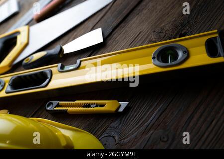 Thema des Auftragnehmers. Werkzeugsatz des Auftragnehmers: Gelber Harthut, libella, Handsäge. Pläne und Notizbuch auf dem rustikalen braunen Plankenhintergrund. Stockfoto