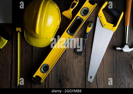 Thema des Auftragnehmers. Werkzeugsatz des Auftragnehmers: Gelber Harthut, libella, Handsäge. Pläne und Notizbuch auf dem rustikalen braunen Plankenhintergrund. Stockfoto