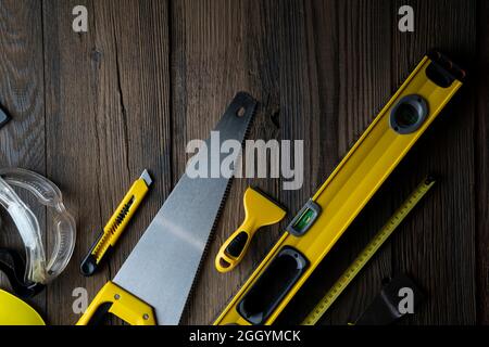 Thema des Auftragnehmers. Werkzeugsatz des Auftragnehmers: Gelber Harthut, libella, Handsäge. Pläne und Notizbuch auf dem rustikalen braunen Plankenhintergrund. Stockfoto