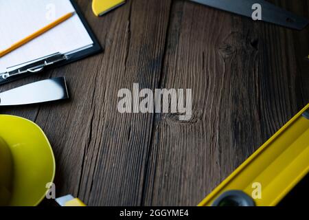 Thema des Auftragnehmers. Werkzeugsatz des Auftragnehmers: Gelber Harthut, libella, Handsäge. Pläne und Notizbuch auf dem rustikalen braunen Plankenhintergrund. Stockfoto