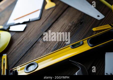 Thema des Auftragnehmers. Werkzeugsatz des Auftragnehmers: Gelber Harthut, libella, Handsäge. Pläne und Notizbuch auf dem rustikalen braunen Plankenhintergrund. Stockfoto