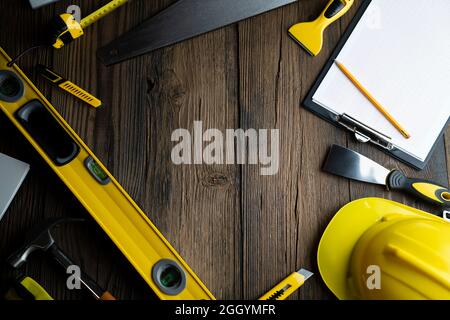 Thema des Auftragnehmers. Werkzeugsatz des Auftragnehmers: Gelber Harthut, libella, Handsäge. Pläne und Notizbuch auf dem rustikalen braunen Plankenhintergrund. Stockfoto