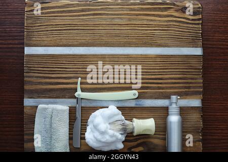 Rasierzubehör auf einem Hintergrund mit Holzstruktur. Werkzeuge. Einweg-Rasierer, Bürste, Rasierer mit Schaumgefahr. Stockfoto
