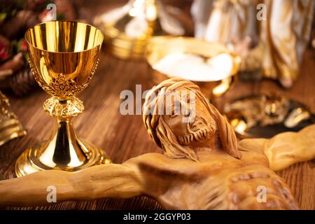 Katholische Symbole Zusammensetzung. Religionskonzept. Jesusfigur, Kreuz, Monstranz, Heilige Bibel, Rosenkranz und goldener Kelch auf dem Holzaltar. Stockfoto