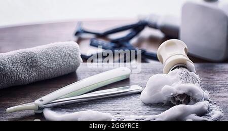 Rasierzubehör auf einem Hintergrund mit Holzstruktur. Werkzeuge. Einweg-Rasierer, Bürste, Rasierer mit Schaumgefahr. Stockfoto