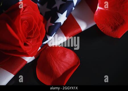 Amerikanische Flagge und Rosenblume auf dem Tisch. Symbol der Vereinigten Staaten von Amerika und rote Blütenblätter. Patriotismus und Erinnerung. Stockfoto