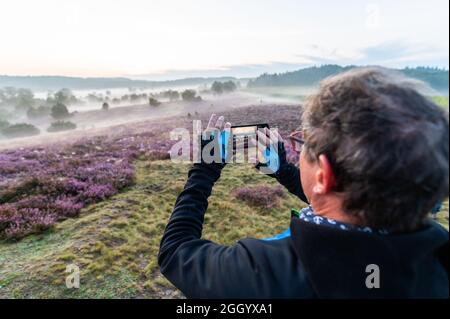 Bispingen, Deutschland. August 2021. Thomas Boschert, Teilnehmer einer E-Bike-Safari, fotografiert in der Lüneburger Heide. Die Fotografin Poliza bietet in den Morgenstunden bei Sonnenaufgang geführte E-Bike-Touren durch die Lüneburger Heide an. Quelle: Philipp Schulze/dpa/Alamy Live News Stockfoto