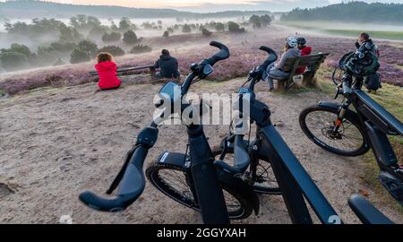 Bispingen, Deutschland. August 2021. Teilnehmer einer E-Bike-Safari genießen den Sonnenaufgang in der Lüneburger Heide. Fotografin Poliza bietet geführte E-Bike-Touren durch die Lüneburger Heide in den Morgenstunden bei Sonnenaufgang an. Quelle: Philipp Schulze/dpa/Alamy Live News Stockfoto