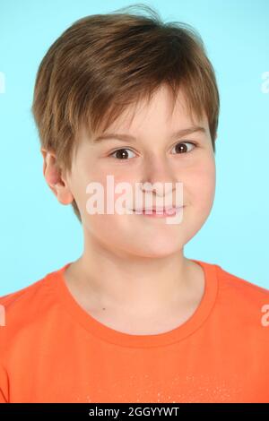 Nahaufnahme Porträt: Ein gut entwickelter, fröhlicher Teenager-Junge in einem orangefarbenen T-Shirt lächelt überrascht und sieht Auge in Auge aus. Stockfoto