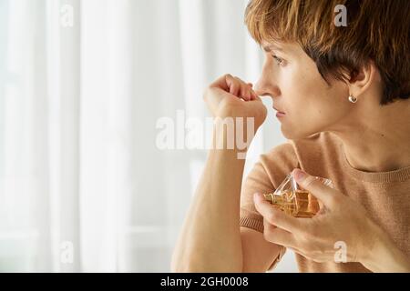 Weibchen versucht, Parfümflasche zu riechen. Geruchsverlust durch sars-Cov-2. Long Covid-Syndrom. Stockfoto