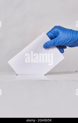 Eine Person in medizinischen Handschuhen wählen. Wahlkonzept. Präsidentschafts- oder Parlamentswahlen. Ein Wähler, der einen Wahlzettel in die Box legt. Wahl Stockfoto