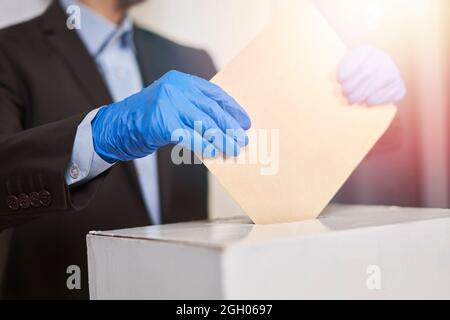 Eine Person in medizinischen Handschuhen wählen. Wahlkonzept. Präsidentschafts- oder Parlamentswahlen. Ein Wähler, der einen Wahlzettel in die Box legt. Wahl Stockfoto