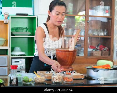 Asiatische Frau trägt Schürze, Kochen in der Küche. Sie bereitet Papaya-Salat zu, ein beliebtes thailändisches Street Food. Stockfoto
