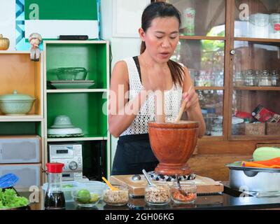 Asiatische Frau trägt Schürze, Kochen in der Küche. Sie bereitet Papaya-Salat zu, ein beliebtes thailändisches Street Food. Stockfoto