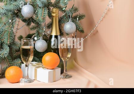 Weihnachten. Eine Neujahrskomposition aus Zweigen eines Weihnachtsbaums, verziert mit silbernen Kugeln, einer Geschenkbox, Sektgläsern, Orangen. Sel Stockfoto