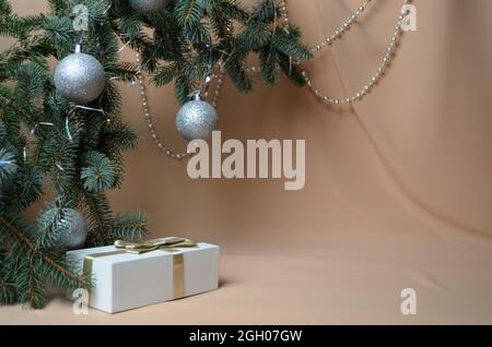 Neujahrsdekoration. Fichtenzweige mit silbernen Kugeln, eine Geschenkbox auf einem beige welligen Hintergrund aus Chiffon. Selektiver Fokus. Stockfoto