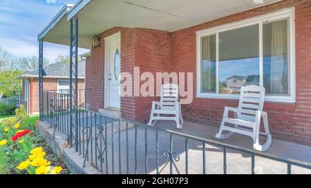 Pano Schaukelstühle auf der Veranda eines Hauses mit roter Backsteinmauer und weißer Tür Stockfoto