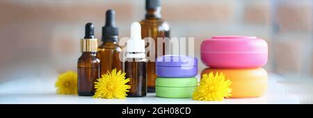 Viele Flaschen und Gläser mit Kosmetika liegen auf dem Tisch mit Gelbe Blüten aus der Nähe Stockfoto