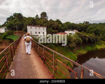 Pilgerin, die über eine steinerne Brücke mit zwei gelben Pfeilen zur Orientierung auf der Route des Camino de Santiago durch Galizien fährt. Stockfoto