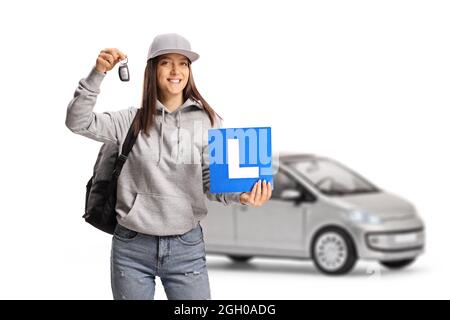 Weibliche Teenager-Studentin, die eine Lernerplatte und einen Autoschlüssel aus einem silbernen Auto auf weißem Hintergrund isoliert hält Stockfoto