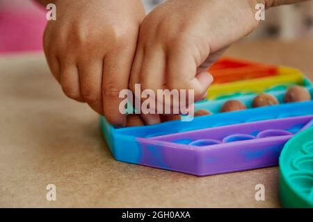 Baby Hands spielt ein Spiel mit Pop-it-Spielzeug und Hasel. Spiel für die Entwicklung der motorischen Fähigkeiten. Der Regenbogen berührt sensorische Fidget. Draufsicht. Hohe Qualität Stockfoto