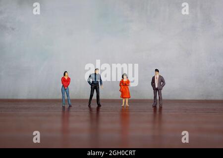 Miniaturmenschen auf Tisch gegen Betonwand mit Kopierraum Stockfoto